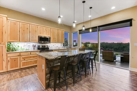 a kitchen with stainless steel appliances granite countertop a stove top oven a sink dishwasher a dining table and chairs with wooden floor