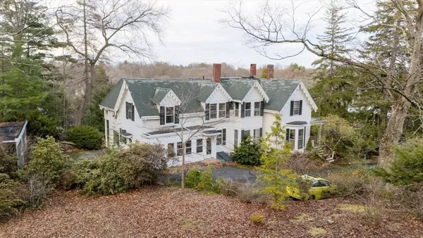a view of a white house next to a yard with large trees