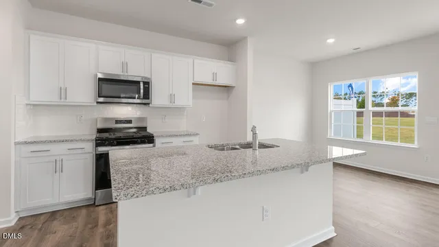 a kitchen with granite countertop a sink a stove a microwave a refrigerator and white cabinets