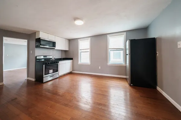 an empty room with wooden floor kitchen view and a window