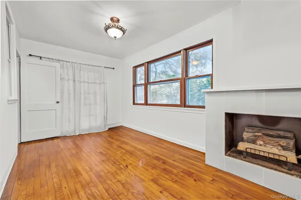 a view of an empty room with wooden floor fireplace and a window