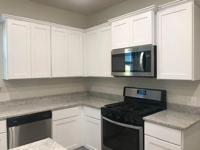 a kitchen with granite countertop white cabinets appliances and a window