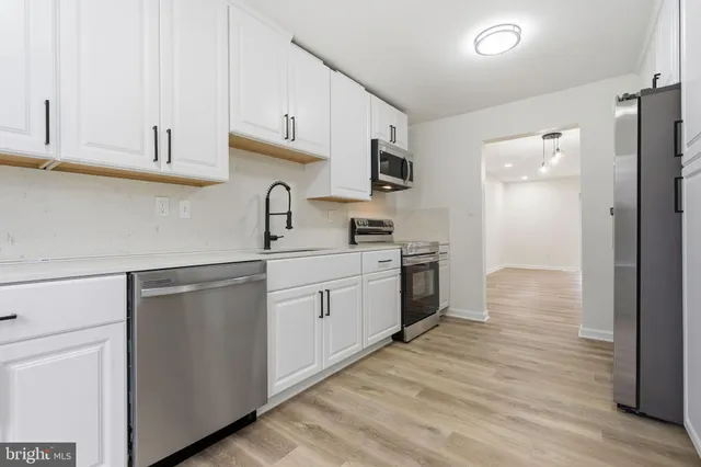 a kitchen with cabinets stainless steel appliances a sink and wooden floor
