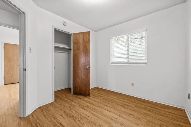 an empty room with wooden floor closet and windows