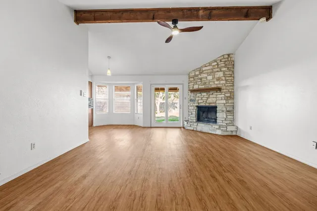 an empty room with wooden floor fireplace and windows