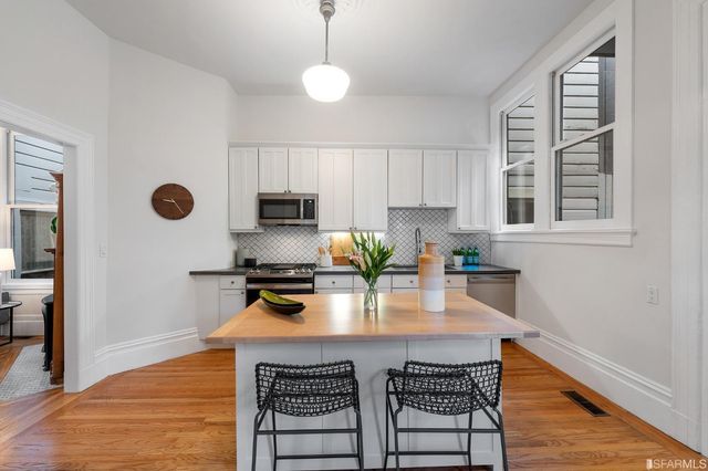 a kitchen with stainless steel appliances granite countertop a stove a refrigerator a sink a stove and white cabinets with wooden floor