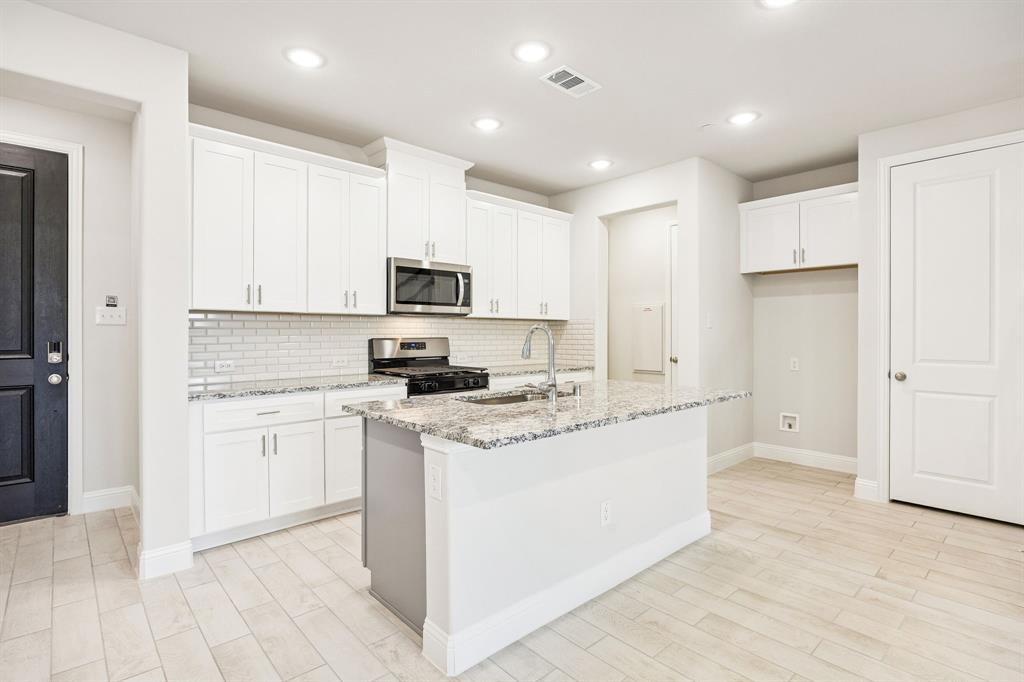 912 Heart Reef Road Plano, TX 75075 - Photo 5 of 20 a kitchen with stainless steel appliances granite countertop a stove top oven a sink a refrigerator and white cabinets with wooden floor