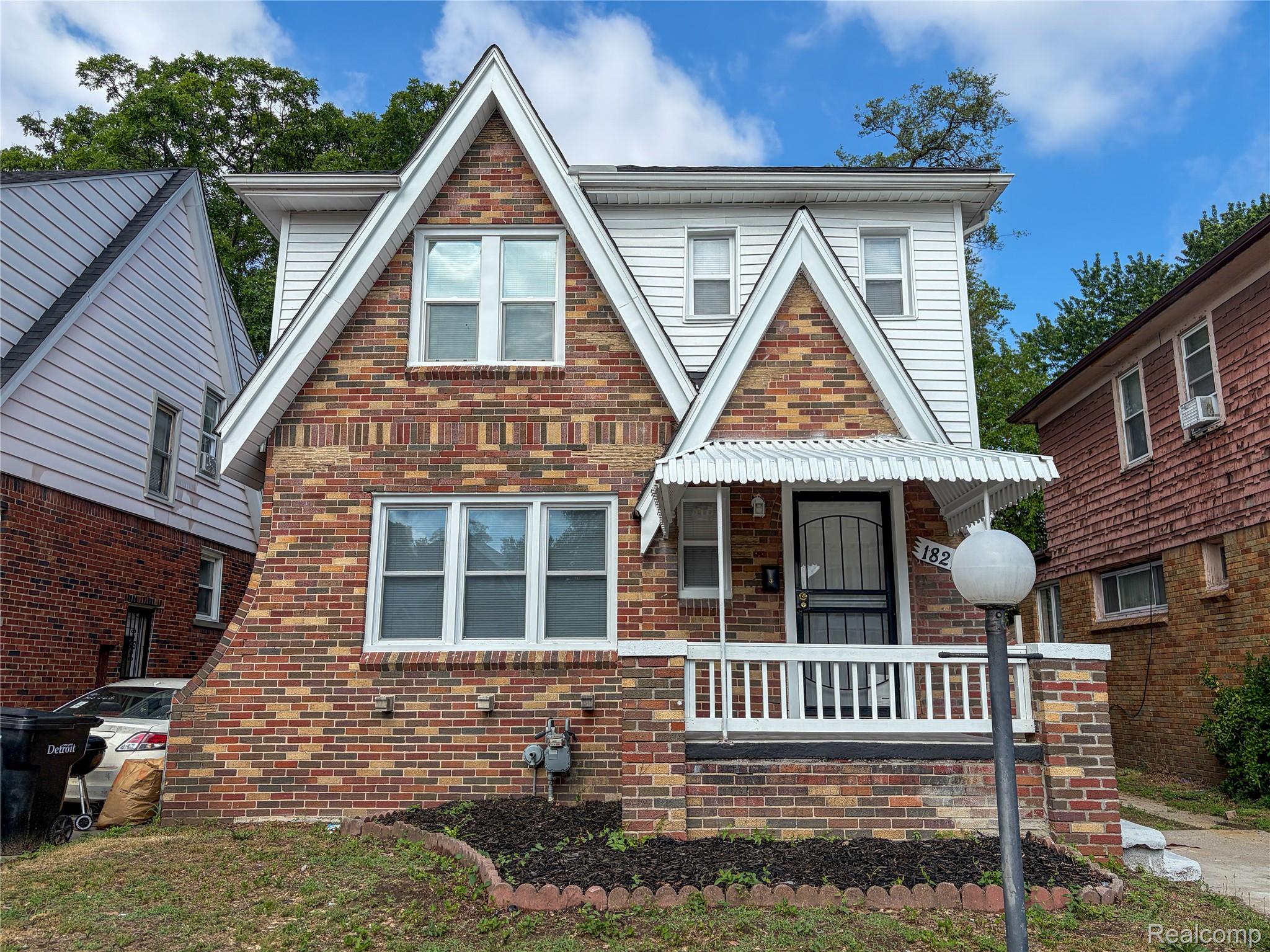 18217 Prairie Street Detroit, MI 48221 - Photo 1 of 34 Brick and siding exterior featuring gabled rooflines, a covered front porch with white railings, and a security screen door