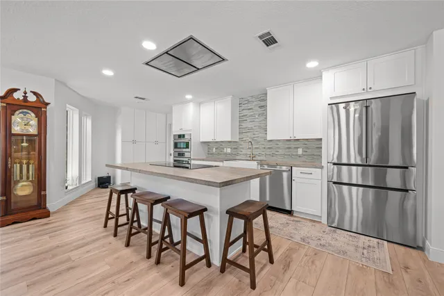 a kitchen with stainless steel appliances granite countertop a refrigerator a sink dishwasher a stove a dining table and chairs with wooden floor