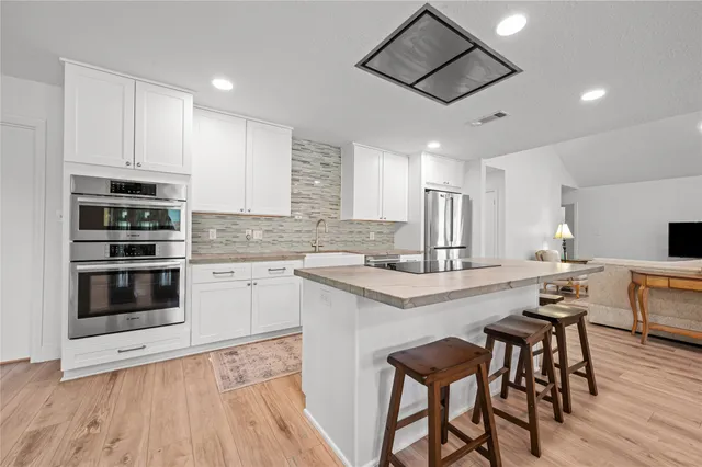 a kitchen with stainless steel appliances a stove a sink dishwasher a refrigerator and white cabinets with wooden floor