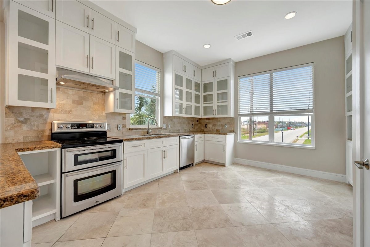1202 Todville Road Seabrook, TX 77586 - Photo 14 of 45 A stylish kitchen showcasing glass-front cabinets, sleek granite countertops, and elegant travertine floors for a timeless and sophisticated look.