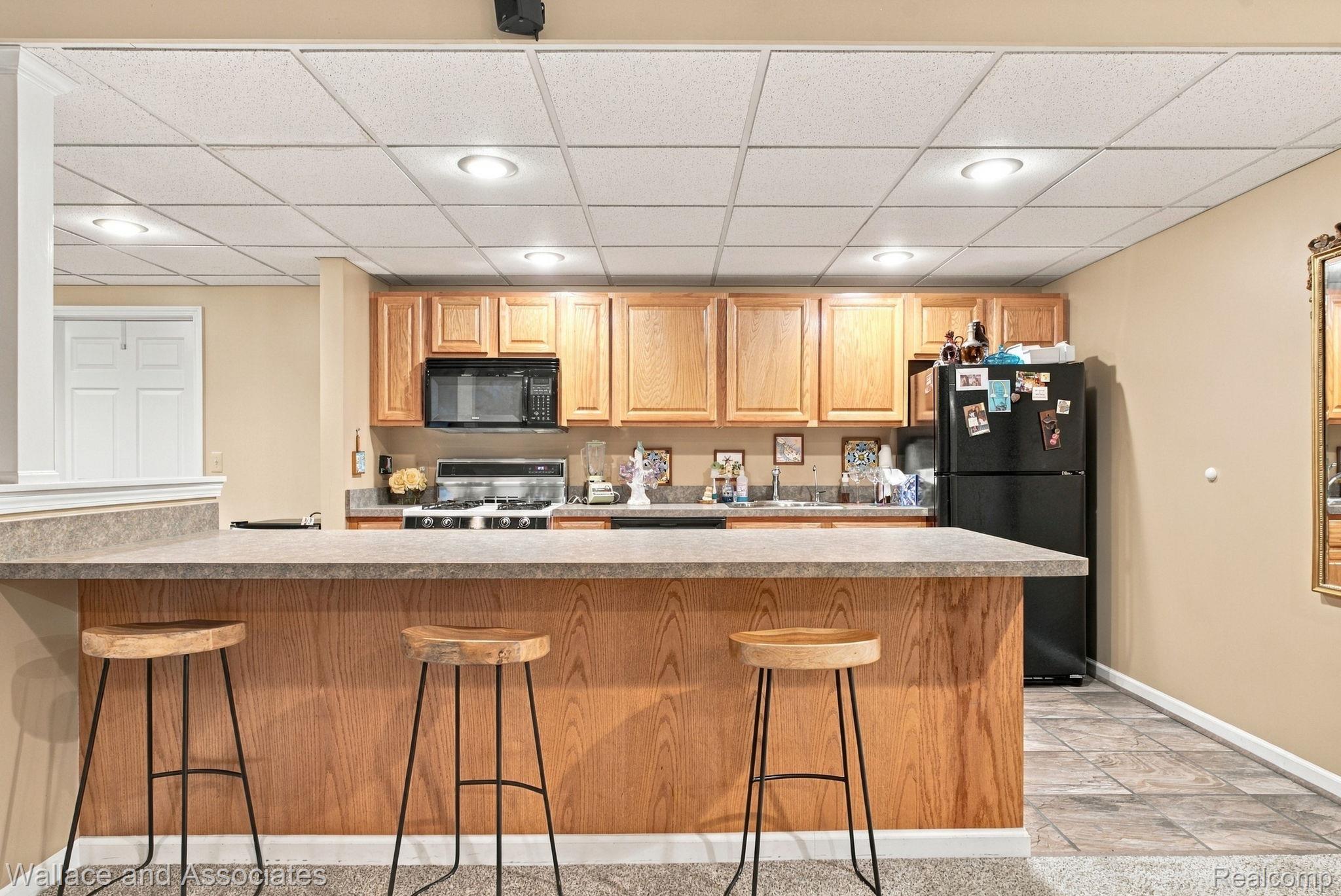 17076 27 Mile Road Ray, MI 48096 - Photo 40 of 63 Kitchenette featuring wood-finish cabinetry, black appliances, a drop ceiling with recessed lighting, and a breakfast bar with a stone-finish countertop