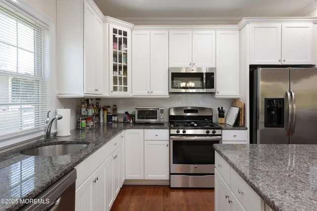 a kitchen with granite countertop a sink stainless steel appliances and white cabinets