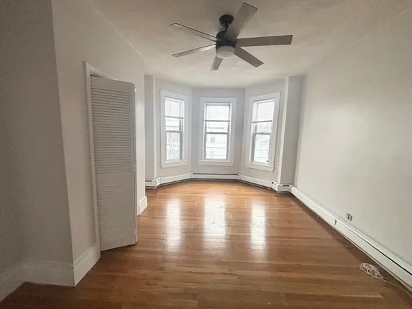 a view of empty room with wooden floor and fan