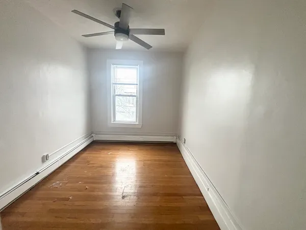 an empty room with wooden floor ceiling fan and windows