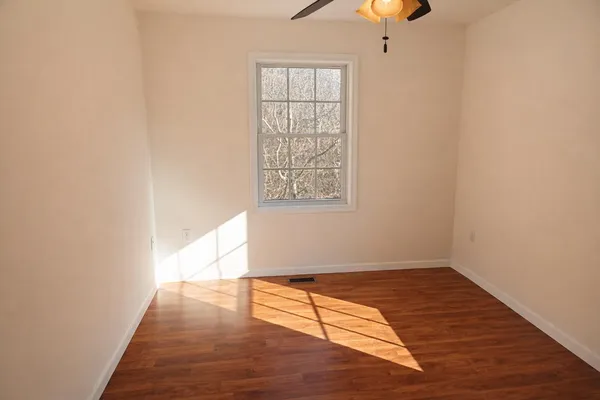 an empty room with wooden floor cabinet and windows