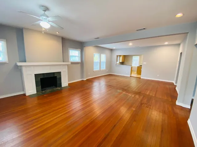 a view of a livingroom with a fireplace a ceiling fan and wooden floor