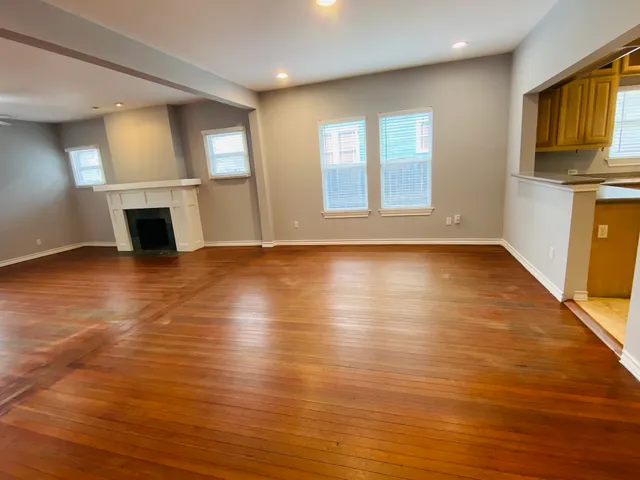 an empty room with wooden floor fireplace and windows
