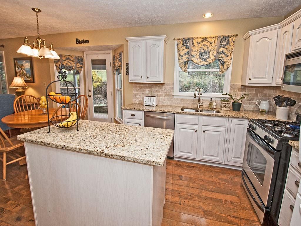 208 Ruth Way McDonald, PA 15057 - Photo 6 of 23 Warm hardwood flooring and granite counters and tile backsplash are perfect combination with the light colored,raised panel cabinetry and stainless appliances. Double stainless sink with gooseneck faucet and over the range microwave offer added convenience. An eating area is situated in a walkout bay window/door area that opens to a covered paver patio. Recessed lighting provides extra light for prep.