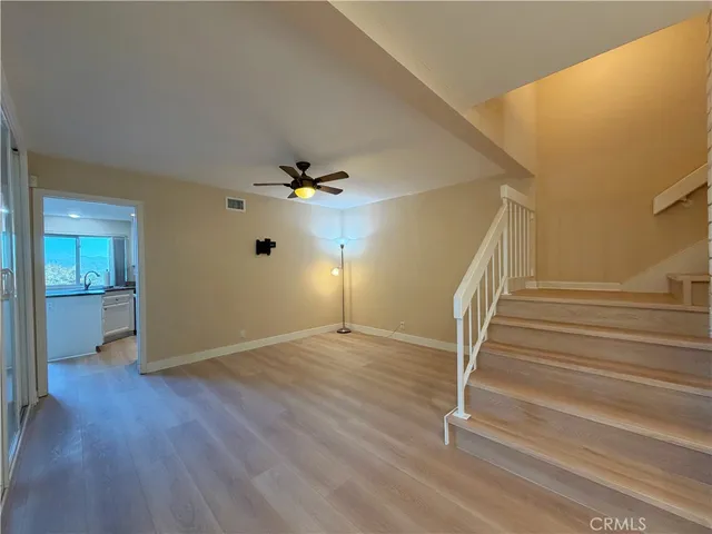a view of an empty room with wooden floor and a ceiling fan