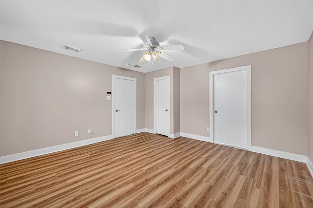 a view of an empty room with chandelier fan and wooden floor