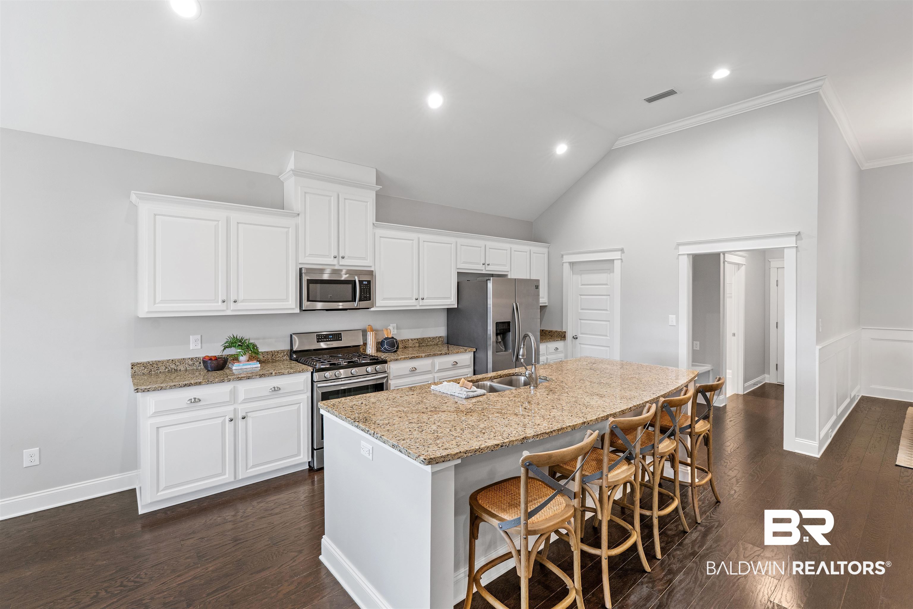 24838 Slater Mill Road Daphne, AL 36526 - Photo 10 of 46 Kitchen featuring appliances with stainless steel finishes, white cabinetry, light stone counters, a kitchen breakfast bar, and dark wood-style flooring