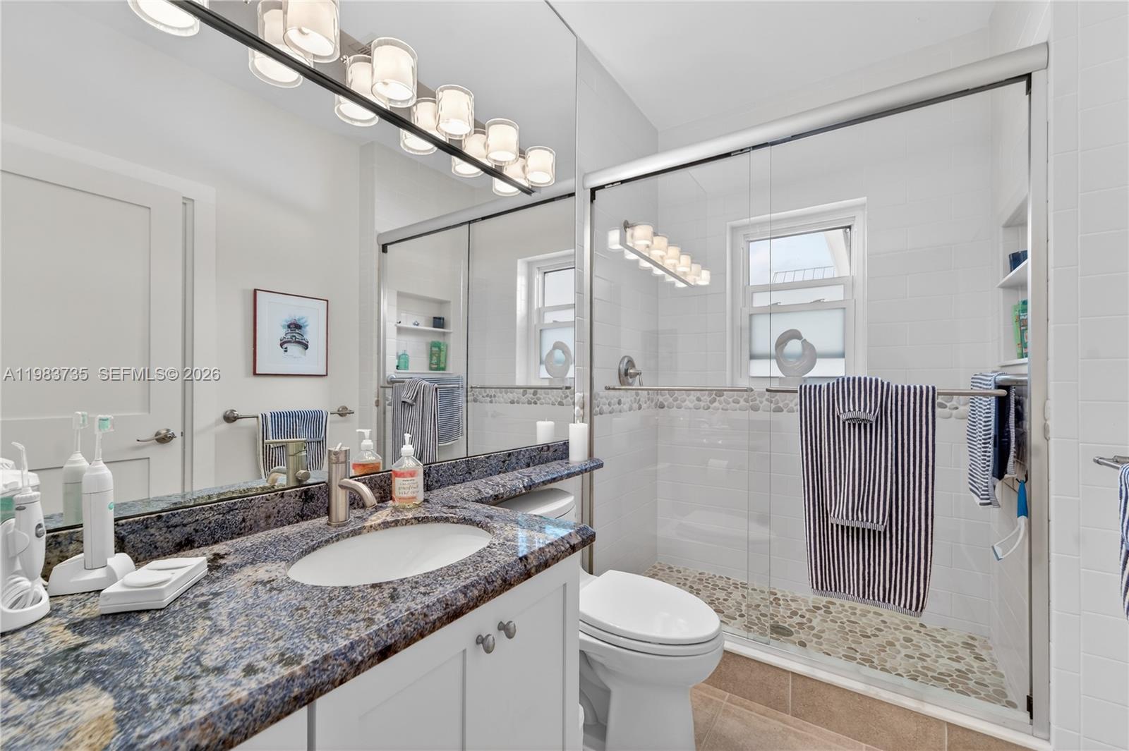 851 Saturn Street, Unit D Jupiter, FL 33477 - Photo 25 of 60 a bathroom with a granite countertop sink a toilet a mirror and shower