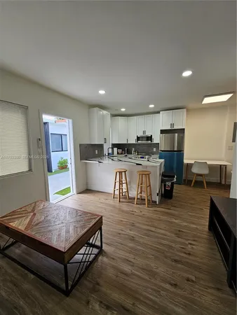 a living room with stainless steel appliances furniture wooden floor and kitchen view