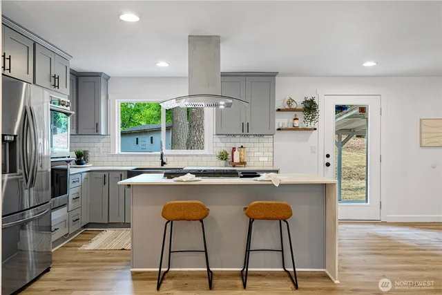 a kitchen with stainless steel appliances granite countertop a stove a sink a refrigerator and white cabinets with wooden floor