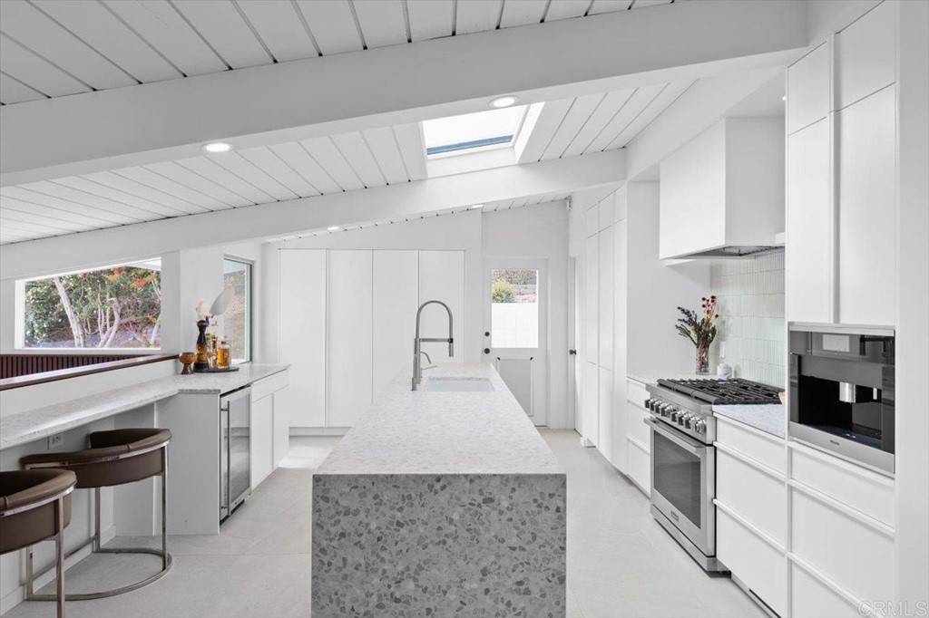 5972 Avenida Chamnez La Jolla, CA 92037 - Photo 2 of 9 a large white kitchen with stainless steel appliances granite countertop a stove a sink dishwasher and white cabinets with wooden floor