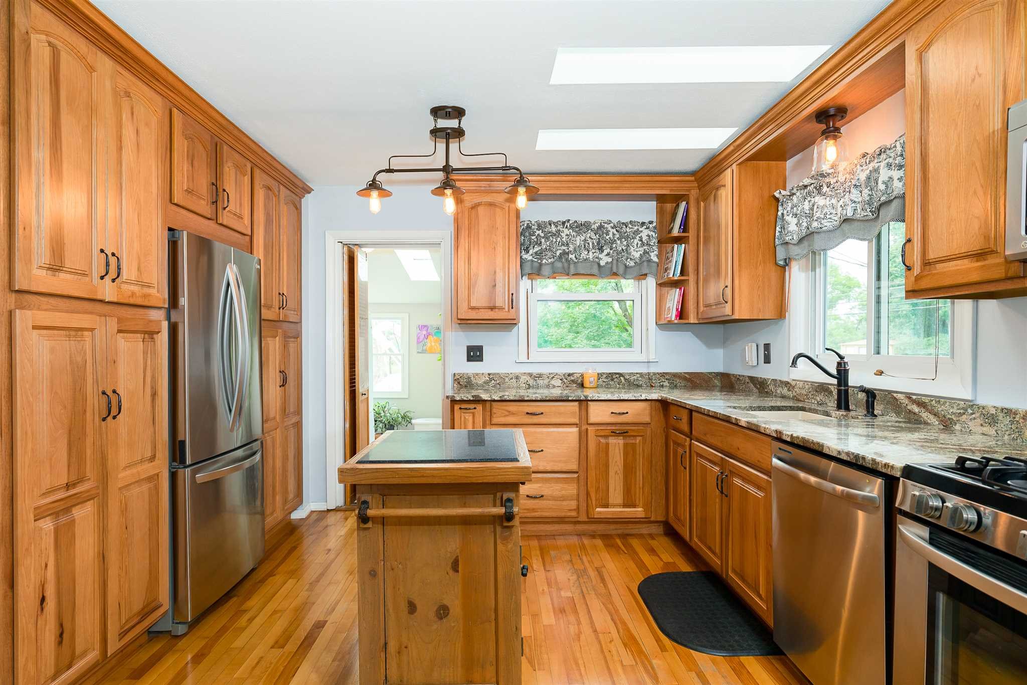 a kitchen with stainless steel appliances granite countertop a refrigerator a sink dishwasher a stove and white countertops with wooden floor