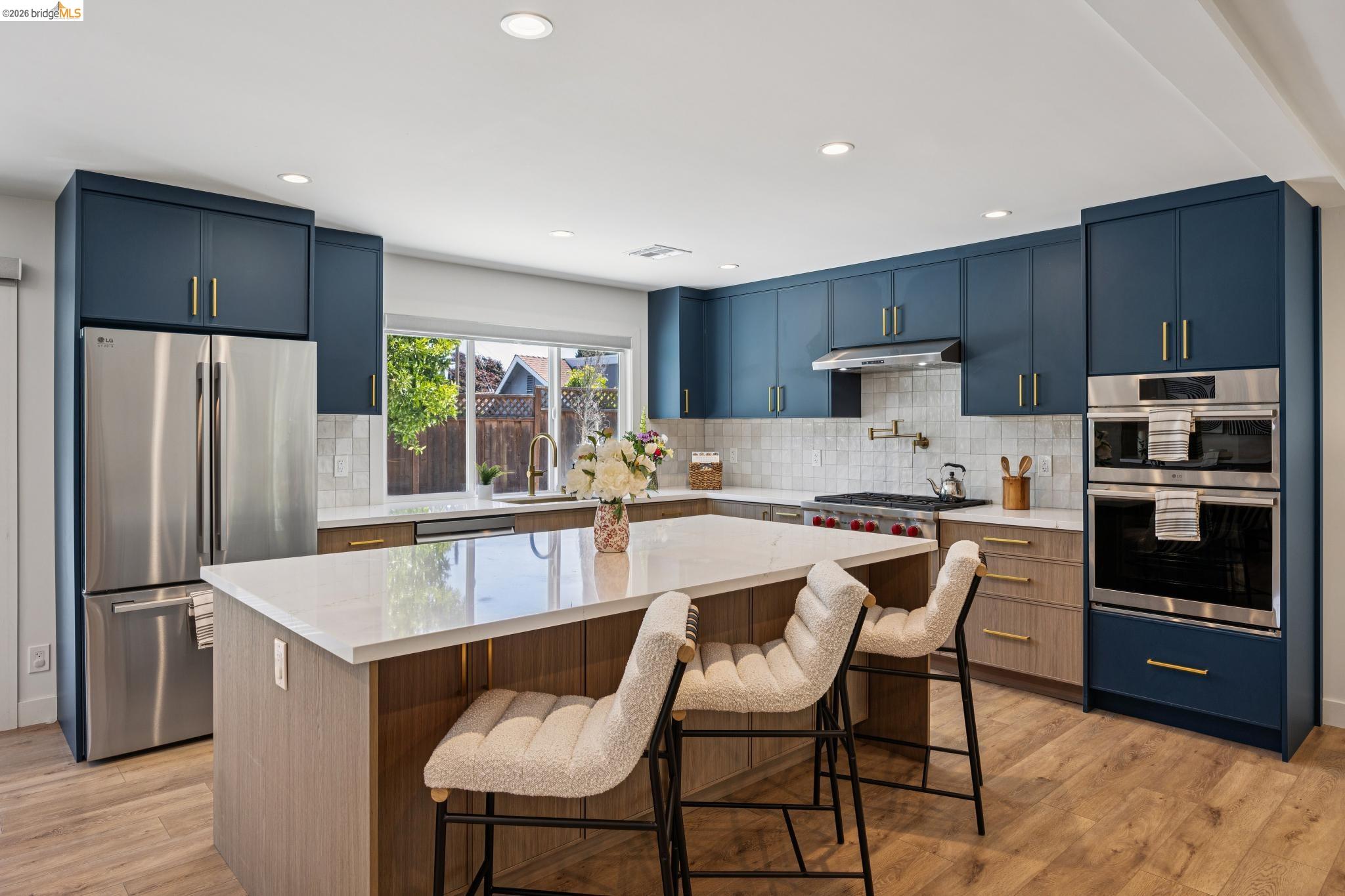 11 Belinda Court San Ramon, CA 94583 - Photo 8 of 33 Kitchen featuring a central island with a light-toned countertop, two-tone cabinetry with gold-finish hardware, stainless steel appliances, and wood-finish flooring