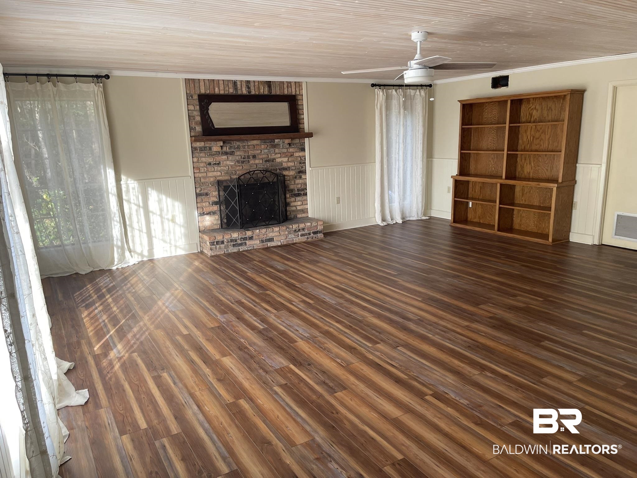 6621 Purvis Road Daphne, AL 36527 - Photo 29 of 59 Unfurnished living room with dark wood-style flooring, ceiling fan, a wainscoted wall, a brick fireplace, and ornamental molding