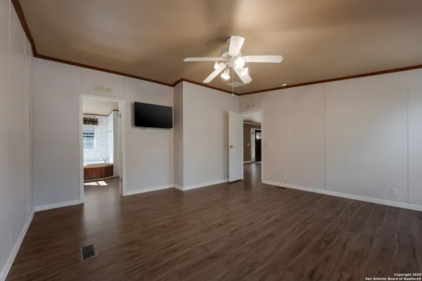 a view of an empty room with wooden floor and a ceiling fan