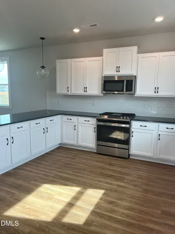 a kitchen with granite countertop a stove a sink and white cabinets