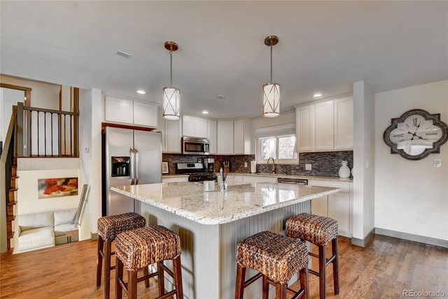 a kitchen with stainless steel appliances granite countertop a stove top oven a refrigerator a sink and a dining table with wooden floor