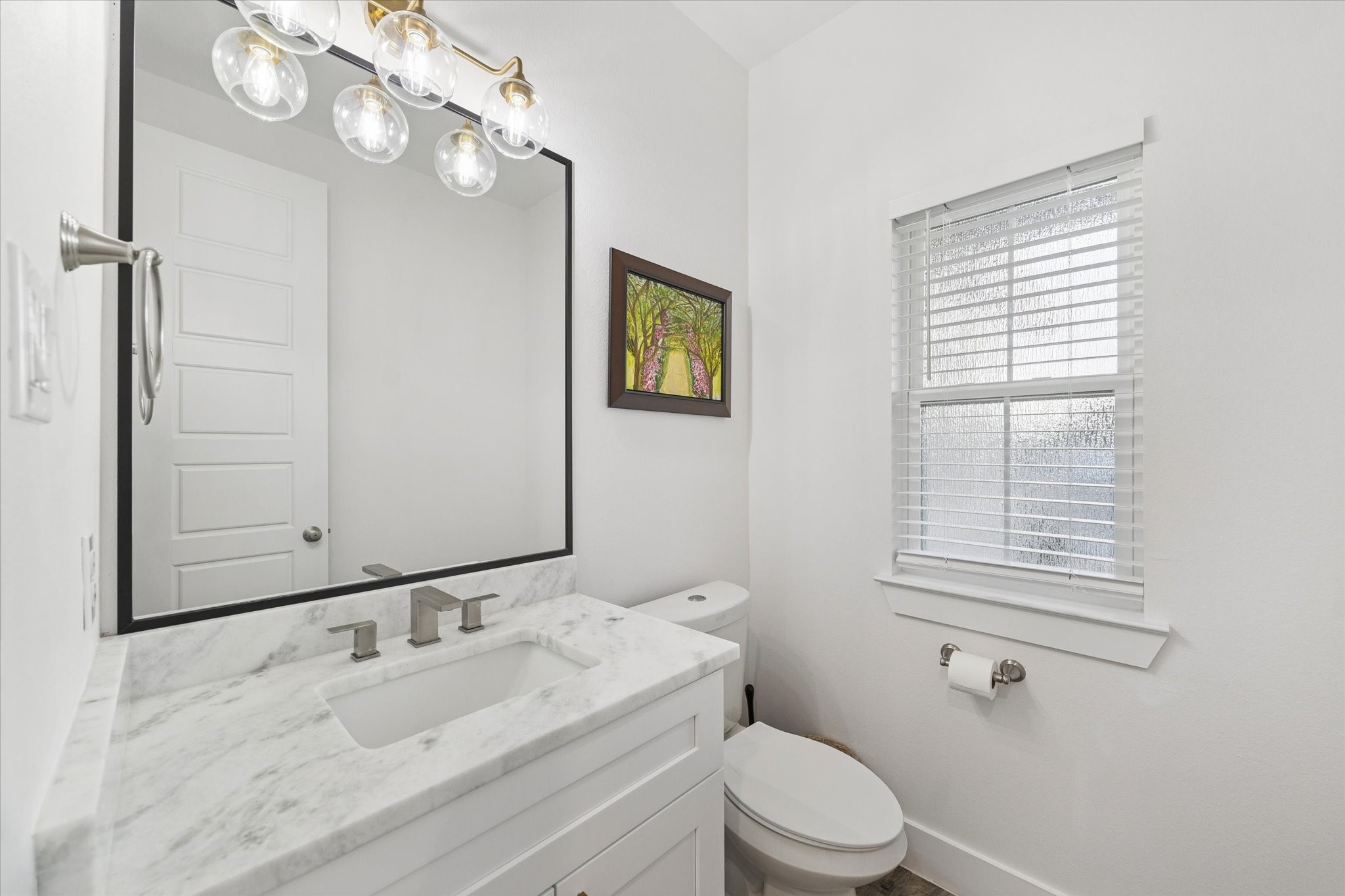 203 Hampton Glen Road Montgomery, TX 77356 - Photo 25 of 35 This powder room features refined details, including a marble countertop, high-efficiency toilet, and custom mirror. The recently installed brass light fixture adds a touch of elegance, while natural light fills the space without compromising privacy, thanks to the designed window glass. A sophisticated and luxurious space for guests, combining style, comfort, and functionality.