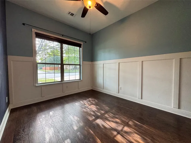 an empty room with wooden floor chandelier fan and windows