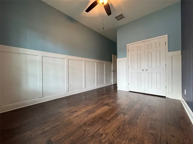 an empty room with wooden floor chandelier fan and windows