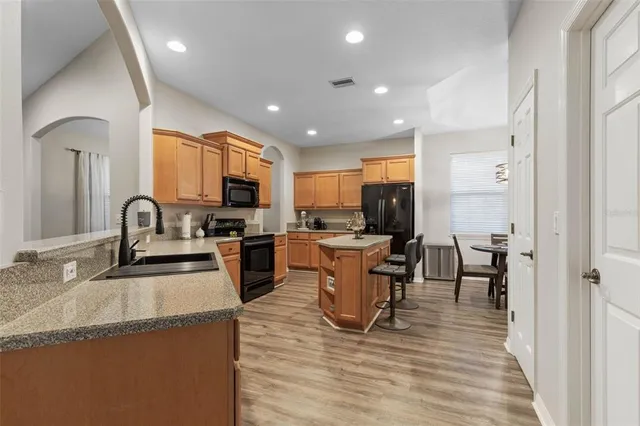 a kitchen with stainless steel appliances granite countertop a sink a stove a refrigerator cabinets and a dining table with wooden floor