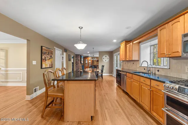 a kitchen with stainless steel appliances granite countertop a refrigerator a sink dishwasher a stove and a dining table with wooden floor