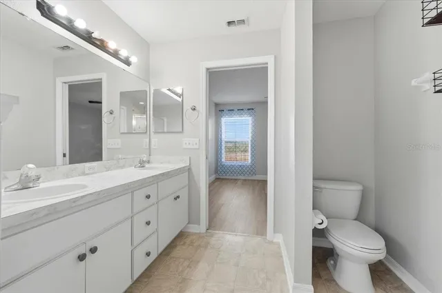 a spacious bathroom with a toilet a double vanity sink and a mirror
