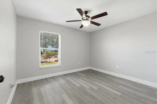 an empty room with wooden floor fan and windows