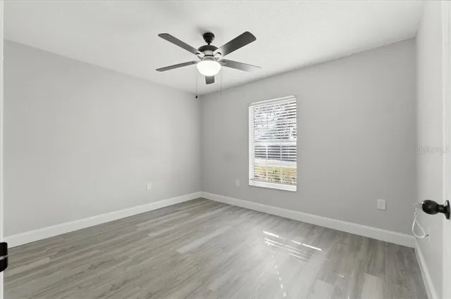 an empty room with wooden floor fan and windows