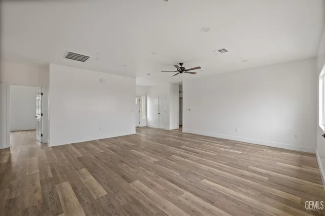 a view of an empty room with wooden floor and a ceiling fan