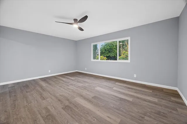 an empty room with wooden floor ceiling fan and windows