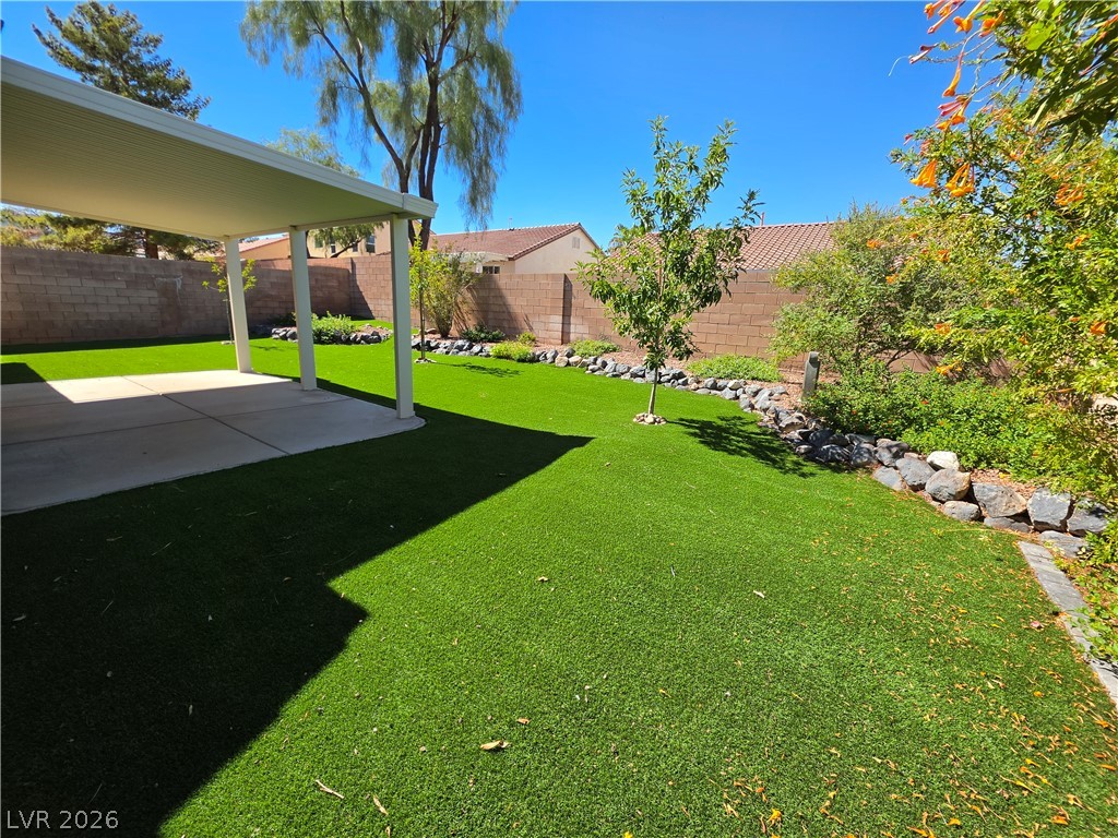 209 Opera House Street Henderson, NV 89012 - Photo 2 of 45 A covered patio overlooks a private, walled backyard featuring artificial turf and rock-bordered garden beds.