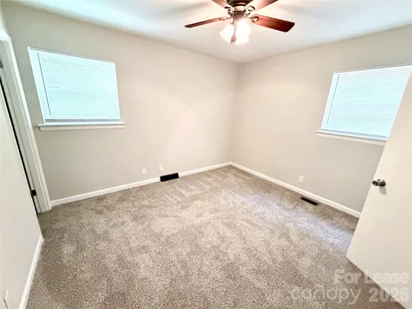 an empty room with a chandelier fan and windows