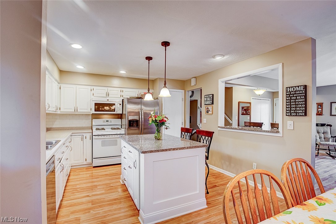 31950 Cannon Road Solon, OH 44139 - Photo 13 of 33 Kitchen with decorative light fixtures, an island with sink, backsplash, white cabinets, appliances with stainless steel finishes, and light hardwood flooring
