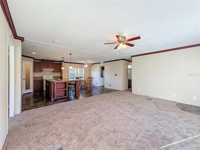 a view of a livingroom with a ceiling fan & a kitchen